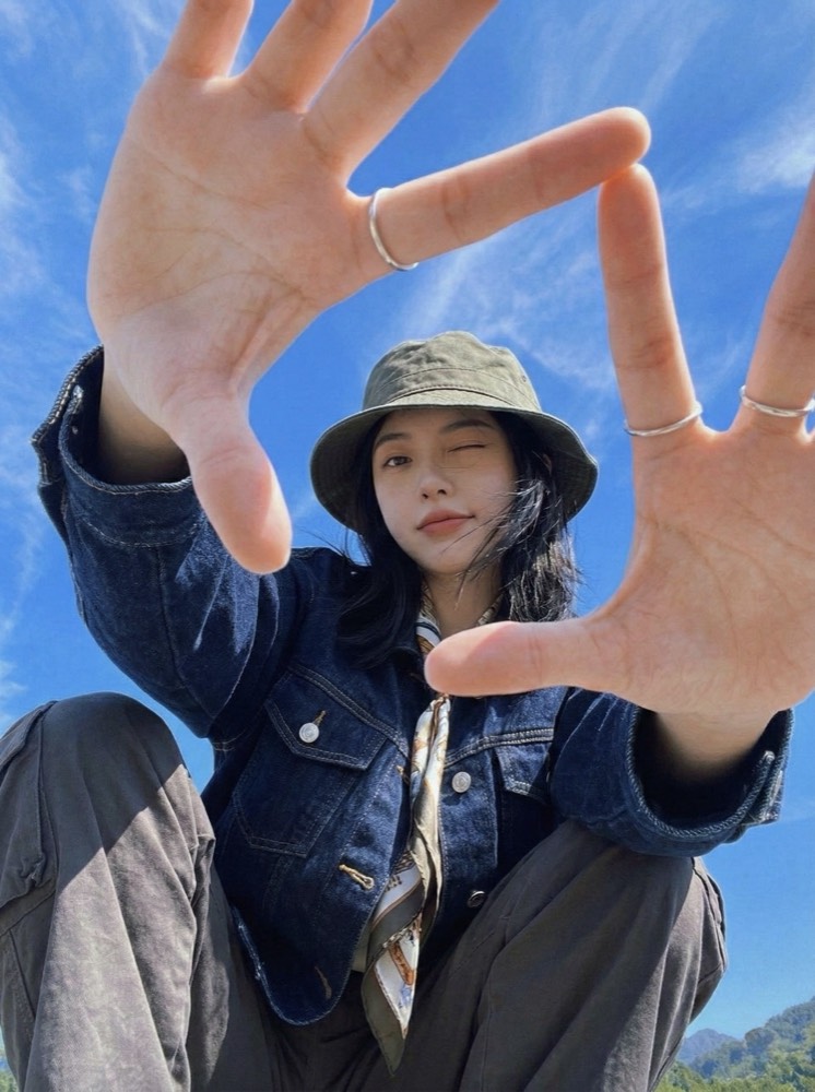 Woman in a denim jacket and bucket hat framing the camera with her hands